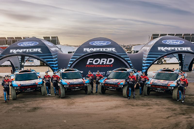 Dakar rally team photo with members standing next to cars