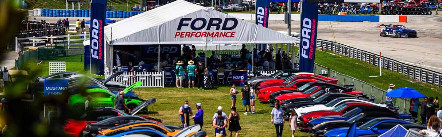 Ford mustang cars around a tent at a motorsports event.