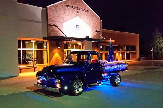 Front profile of blue 1955 F-100 Stakeside Platform Flatbed parked in front of building