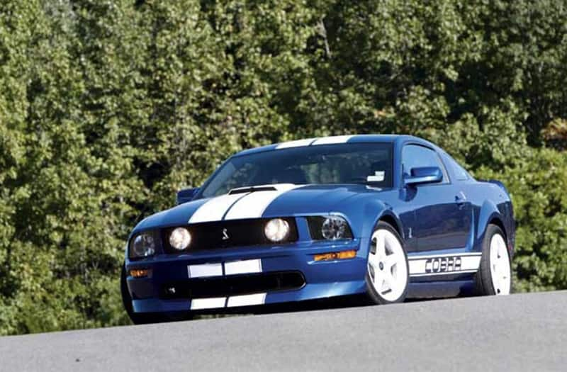 Front view of the Honorary 2005 Mustang Cobra driving on road with trees