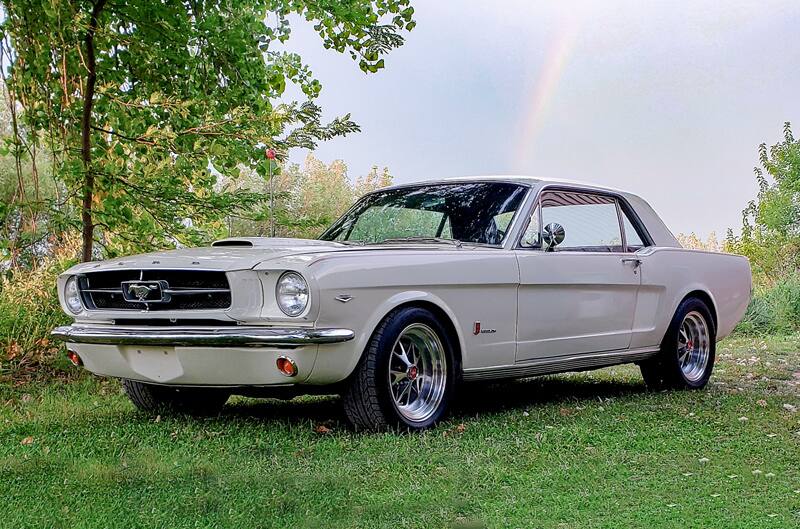 Driver side view of Wimbledon White 1965 Mustang GT parked on grass with rainbow in background