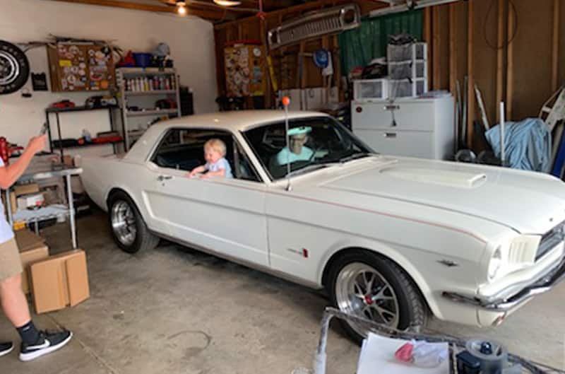 Adam Gillespie's father and son sitting inside of his grandfathers Wimbledon White 1965 Mustang GT parked in garage