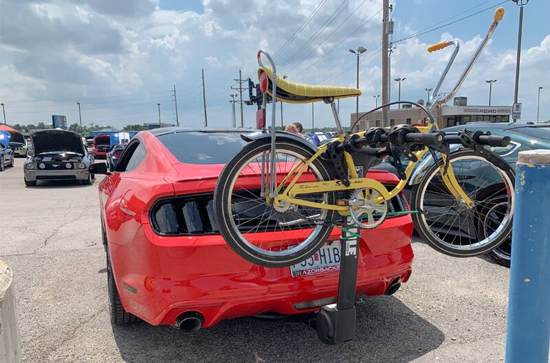 Rear view of parked red 1965 Mustang Fastback with yellow bike attached to the back