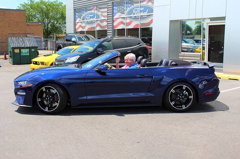 Profile of Kona blue Mustang with Dennis Healy in it in the parking lot