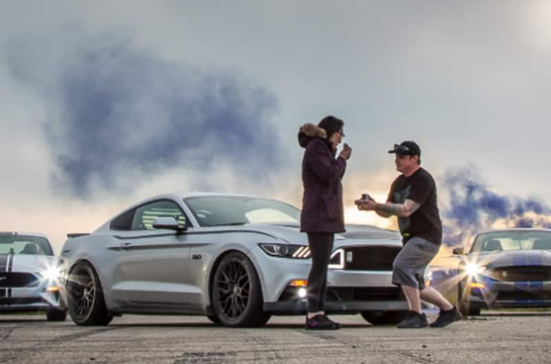 A man proposing to a woman in front of Mustangs