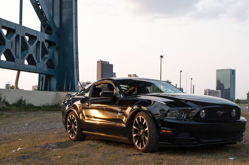 Front profile of black Mustang GT parked on grass next to bridge