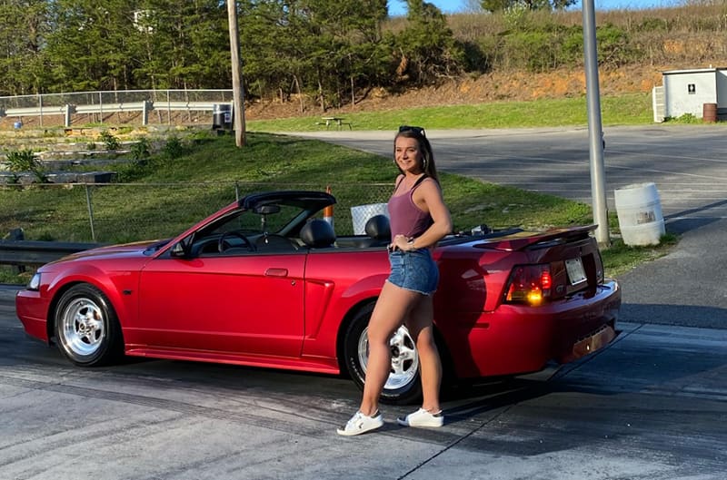 Bailey standing with her 2000 Ford Mustang GT in Lazer Red