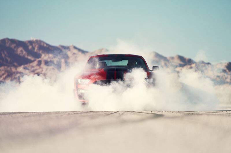 A red and black Mustang kicking up smoke during its burn out