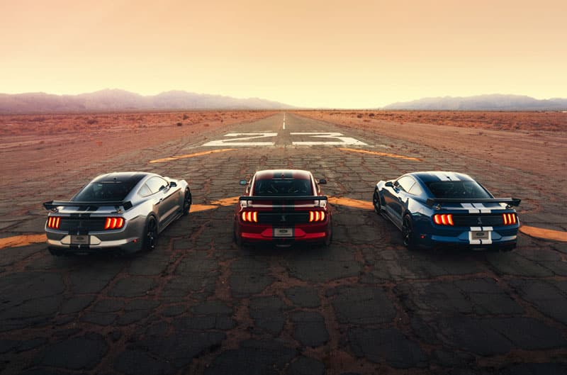 A rear view of a red, a blue and a grey Mustang on the road