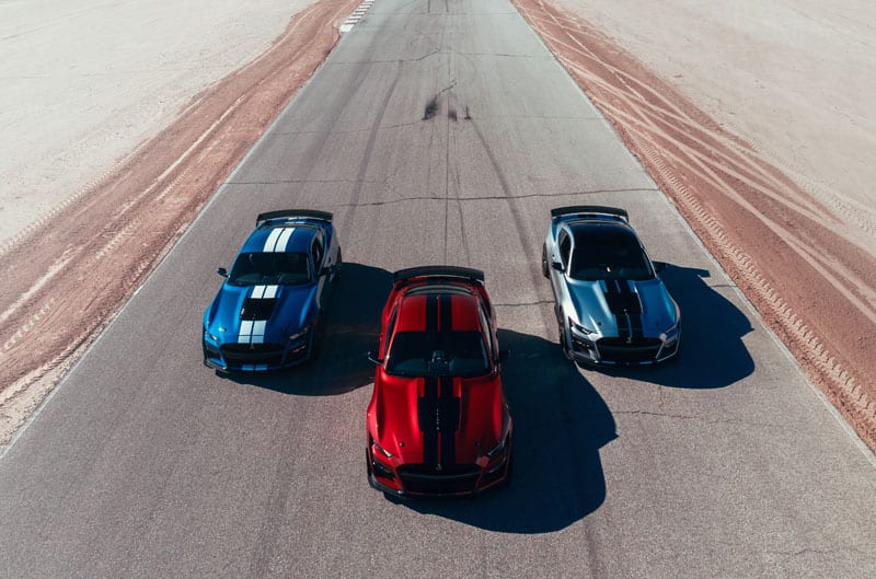 Grey, red and blue Mustangs driving down the road