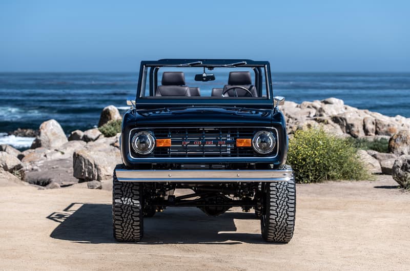 A front end view of a custom blue Ford Bronco with a lake in the background