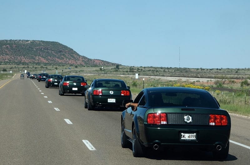 Several Bullitt Mustangs in highland green are pictured driving on Route 66 to the Friends of Steve McQueen show