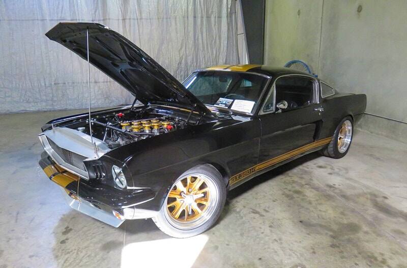 A front side view of a black Mustang on display with the hood up