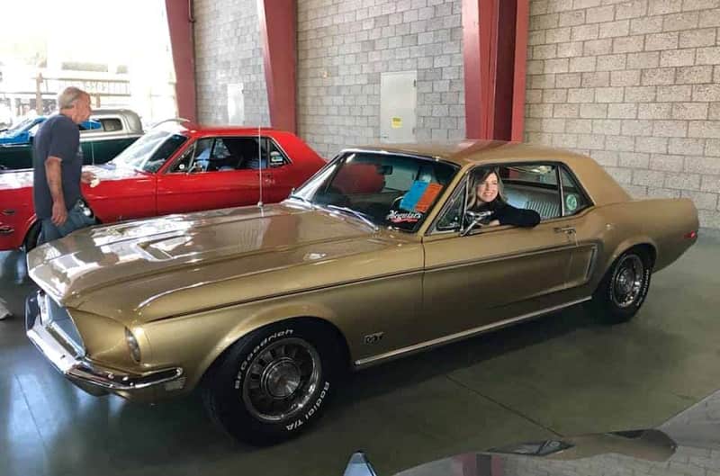 A side view of a woman inside a classic brown Mustang on display
