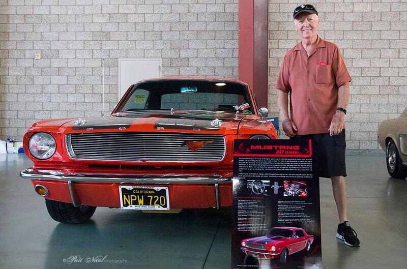 A man taking a photo with a red and black Mustang on display