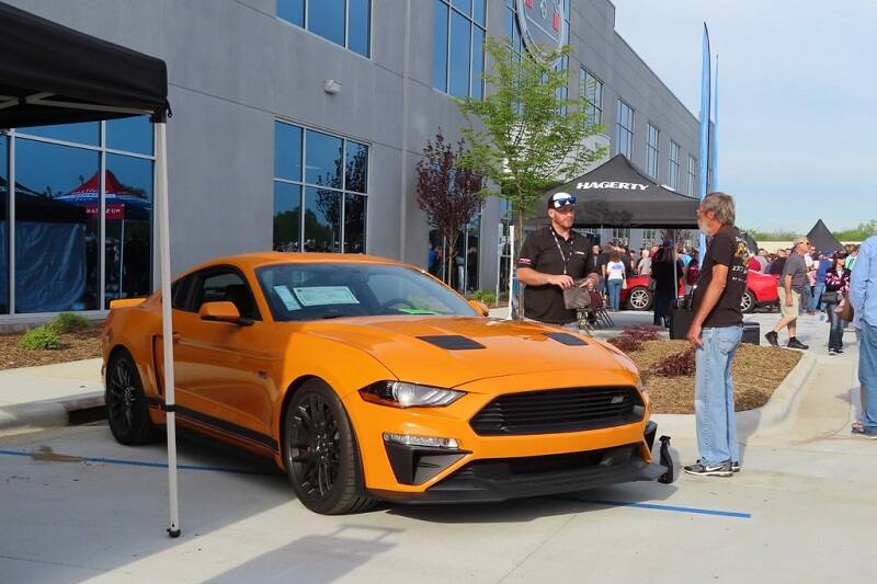 Front of orange Mustang parked in lot with two men standing next to it