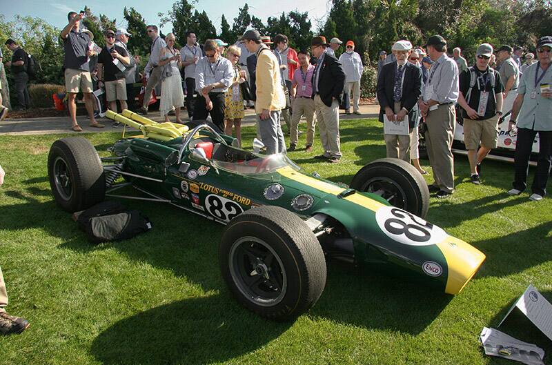 A group gathered around a small green and yellow Ford Lotus racecar