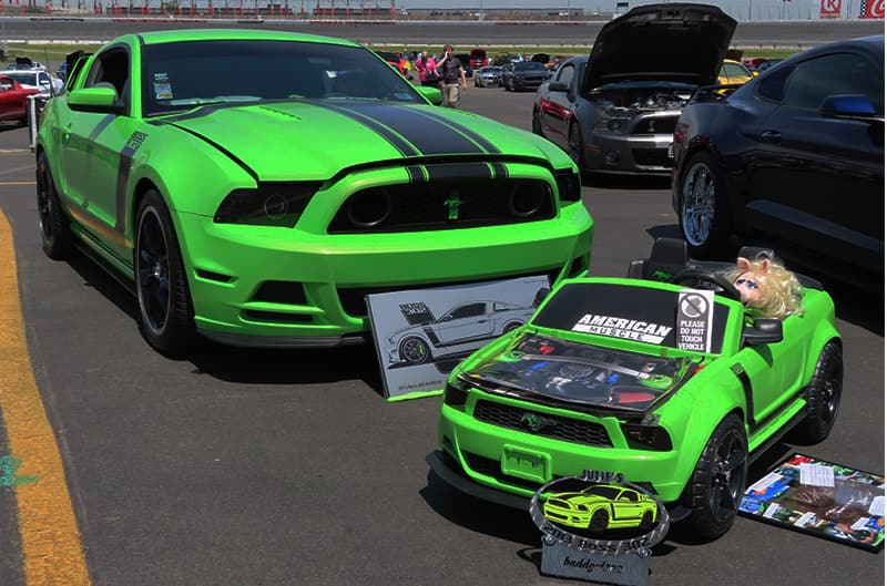 A miniature green and black Mustang sitting in front of the real green and black Mustang