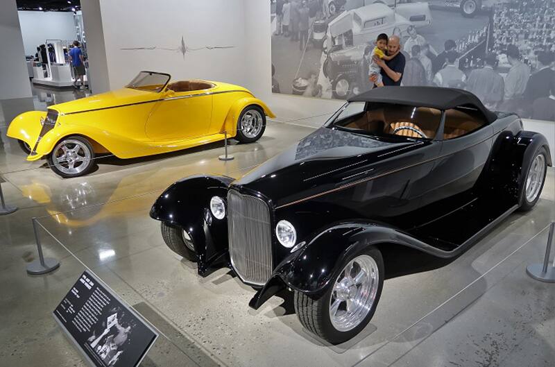 A man and a child admiring a classic black vehicle on display