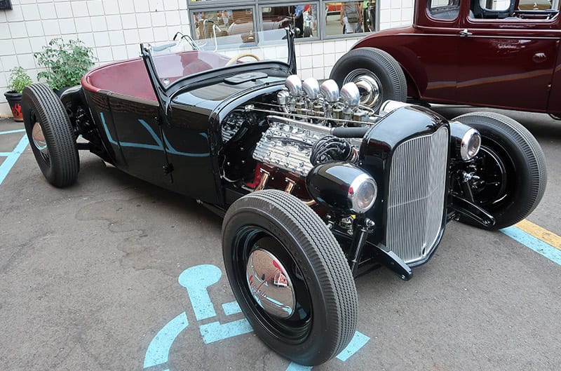 Front profile of a black classic Ford with roof down in parking lot