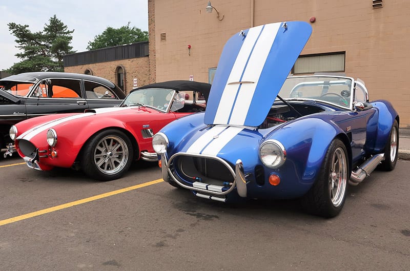 Front of blue Shelby Cobra with white stripes on open hood in parking lot