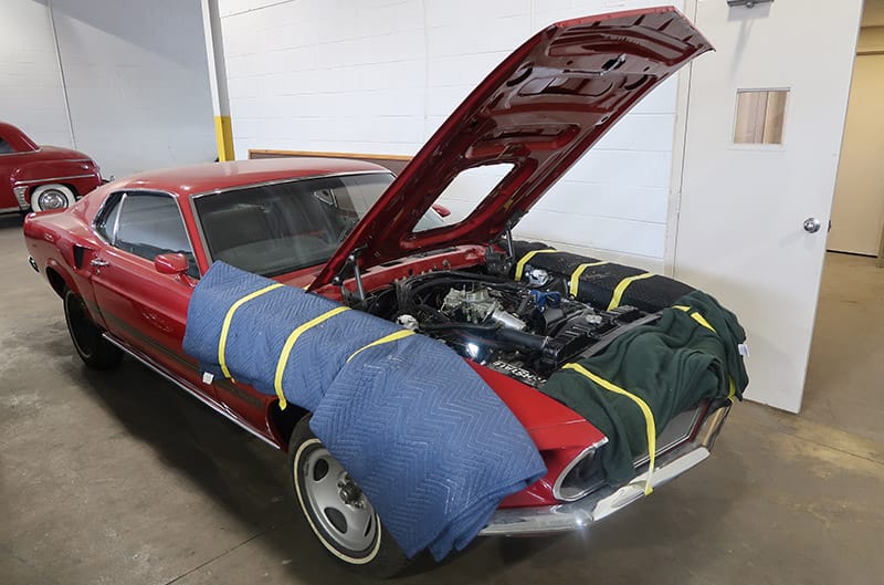 Front profile of red Mustang with hood open in garage