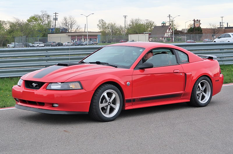 A side view of a red Mustang being driven down the road