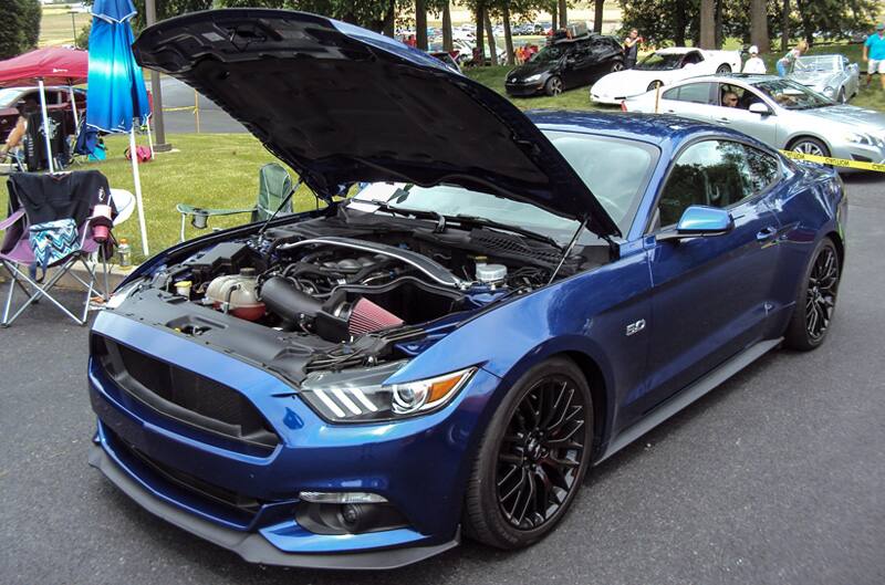 Front profile of a blue Mustang with hood open in the parking lot