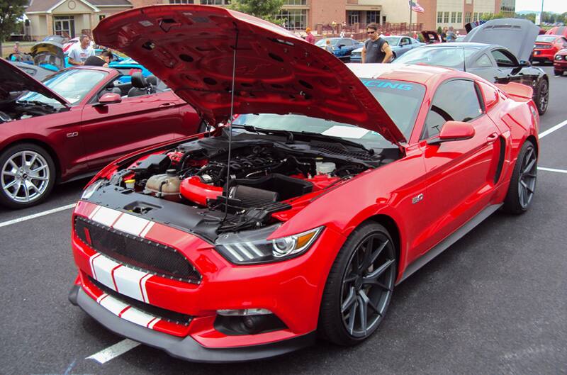 Front profile of a red Mustang with white stripes on open hood in parking lot