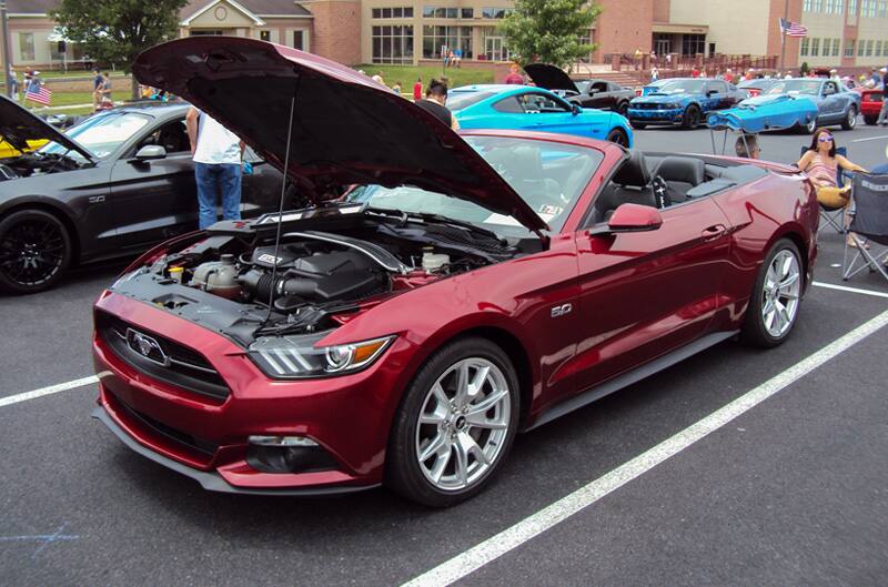 Front profile of a red Mustang with hood open in the parking lot