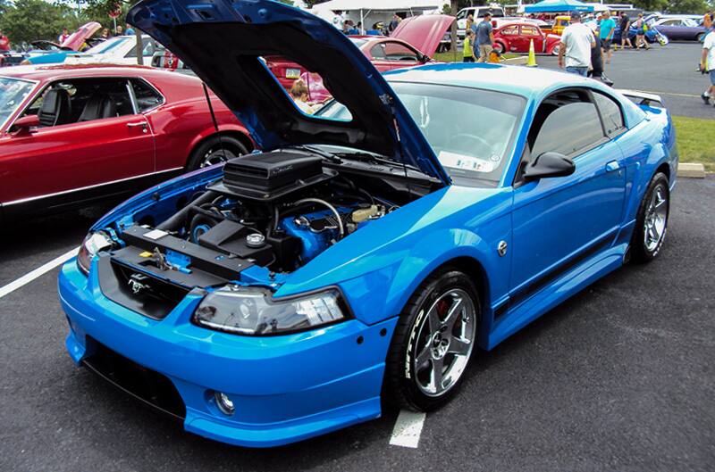 Front profile of a blue Mustang with hood open in the parking lot