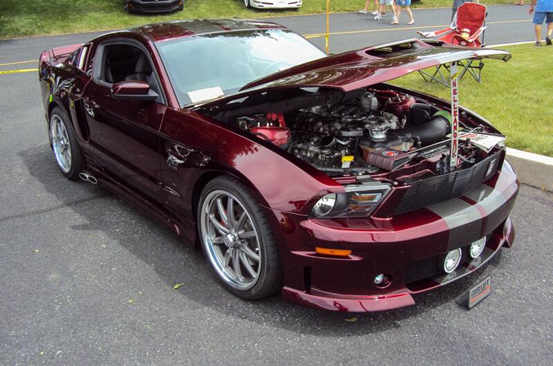 Front profile of a burgundy Mustang with gray stripes on open hood in the parking lot