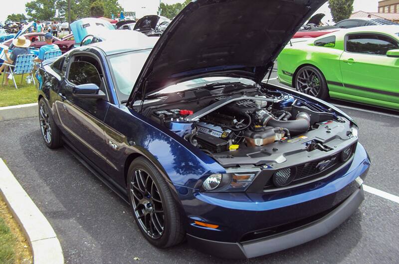 Front of a blue Mustang with hood open in the parking lot