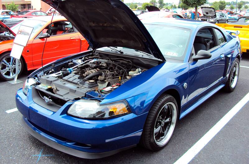 Front profile of a blue Mustang with hood open in the parking lot