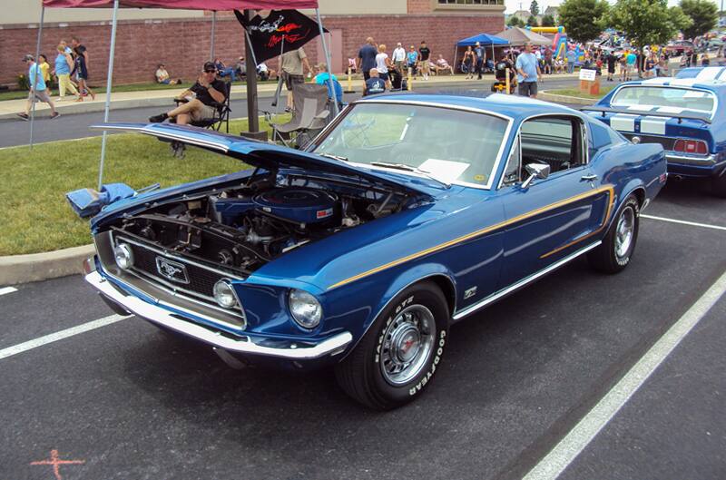 Front profile of a blue Mustang with hood open in the parking lot