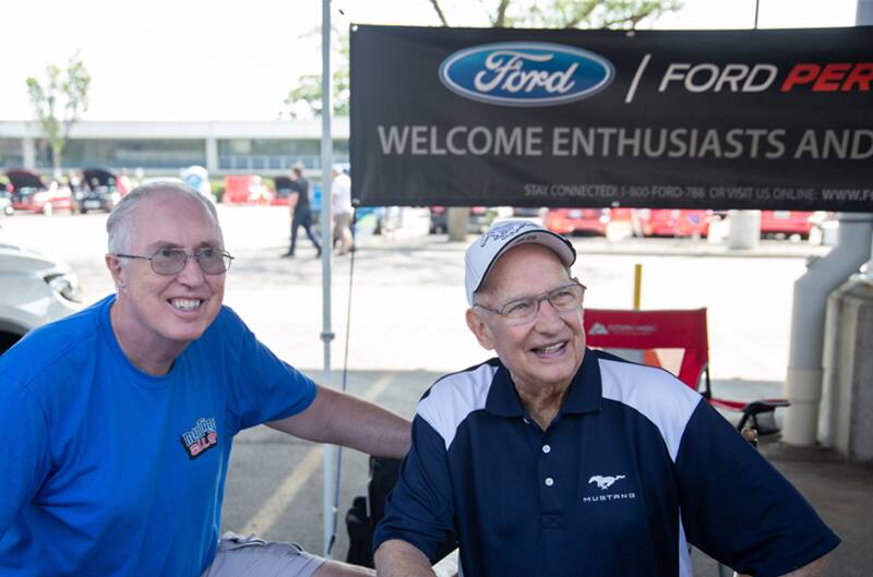 Two men posting for the picture in front of a Ford Performance sign in the parking lot