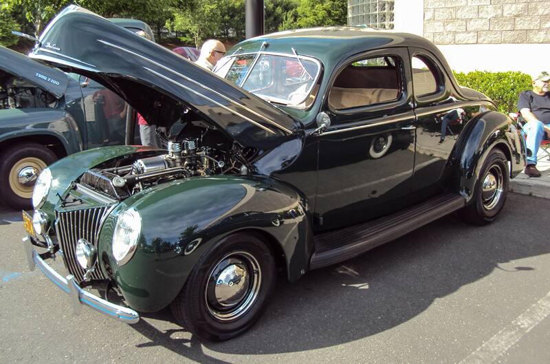 Front profile of a green classic Ford car with hood open in parking lot