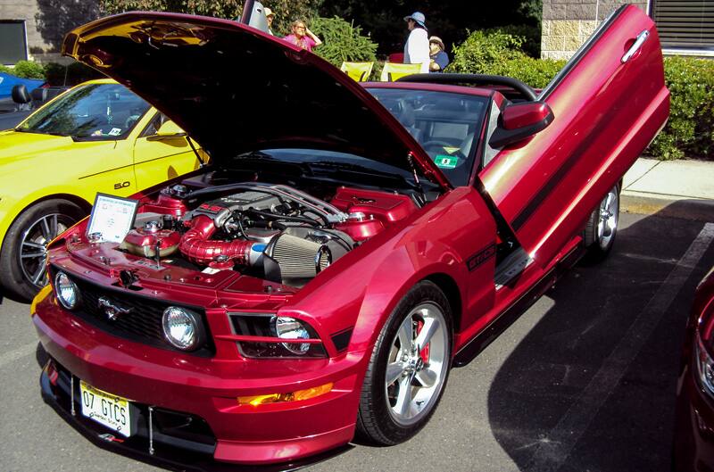 Front of a red Mustang with hood and door open in parking lot