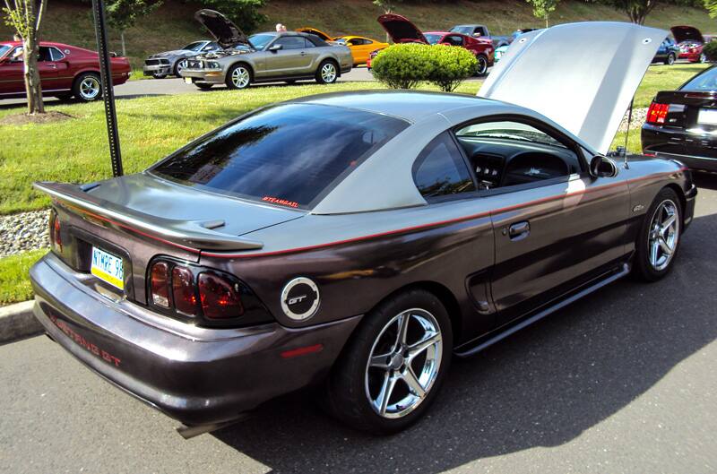 Rear profile of a gray Mustang GT with hood open in parking lot