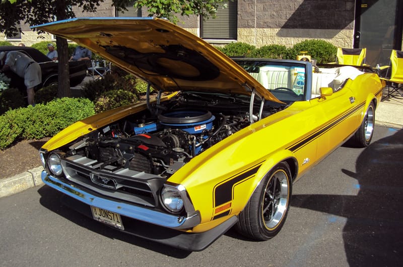 Front of a yellow Mach 1 convertible with hood open in parking lot