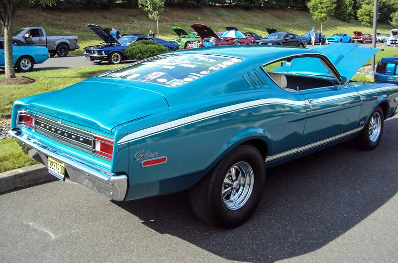 Rear of a teal Mercury with hood open in parking lot