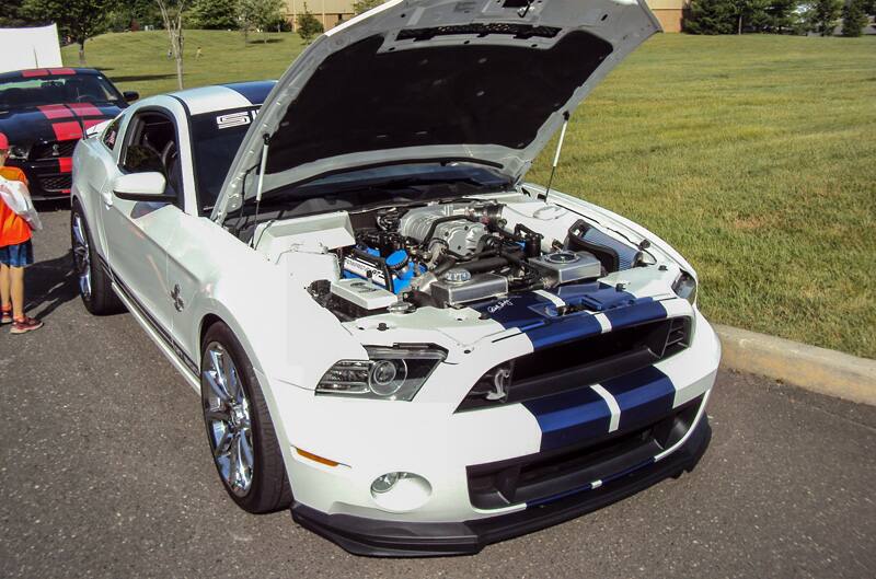 Front of a white Shelby with blue stripes and hood open in parking lot