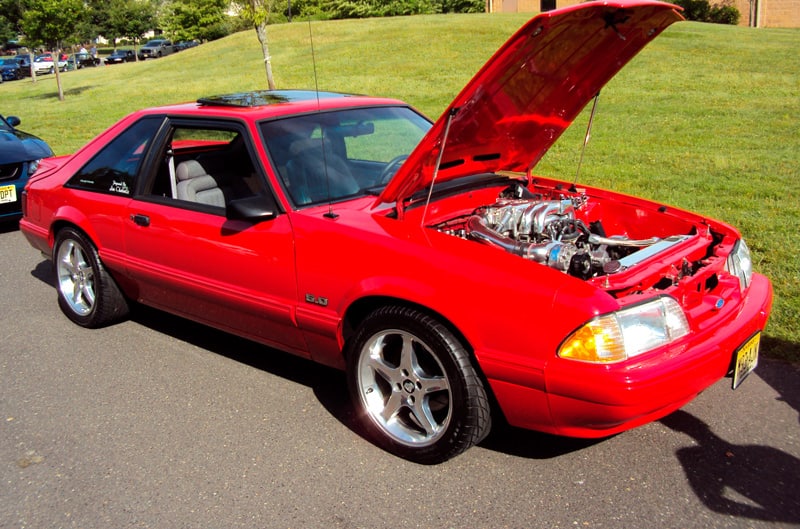 Front profile of a red Mustang with hood open in parking lot