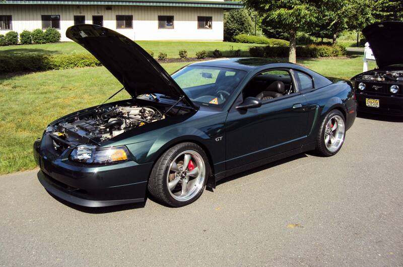 Profile of a black Mustang GT with hood open in parking lot