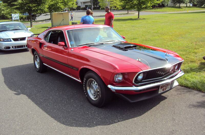 Front of a red Mach 1 with black stripe on hood in the parking lot