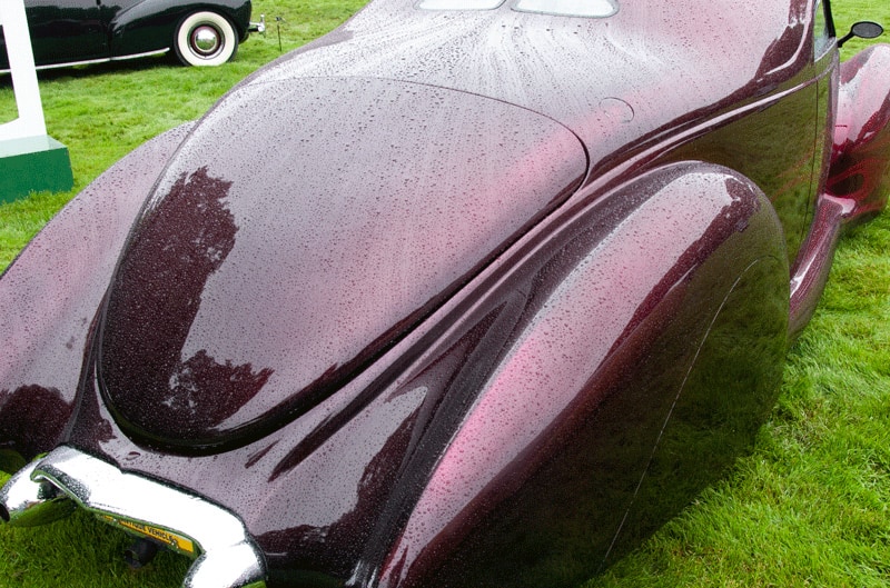 A rear side view of a classic purple vehicle on display