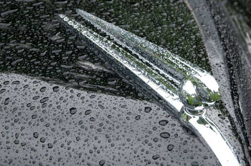 A closeup of the front hood of a classic vehicle covered in rain droplets
