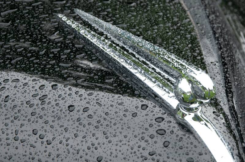 A closeup of the front hood of a classic vehicle covered in rain droplets