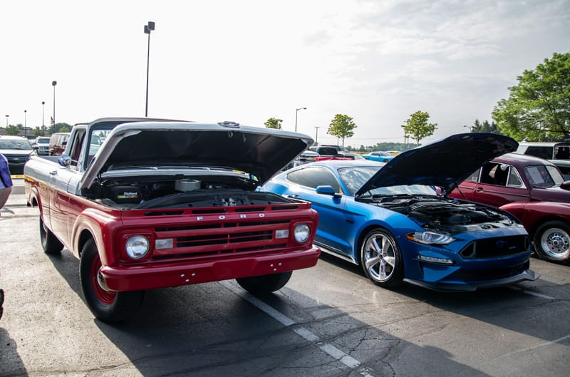 A front side view of a red and black Ford truck on display with the hood up