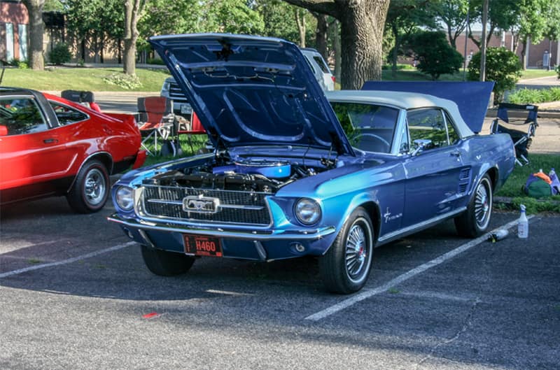A front side view of a classic blue Mustang on display with the hood and trunk open